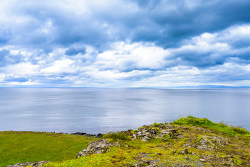 Beautiful rugged volcanic basalt rock Iceland coastline blue skies and low clouds. Green moss and grass covered hills.