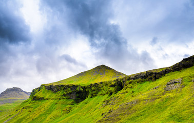  Beautiful rugged volcanic basalt rock Iceland highlands with fog and rain against blue skies with low clouds. Green moss and grass covered hills and plains.  