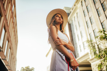 Young woman in hat walks at city street on background of buildings and sky.