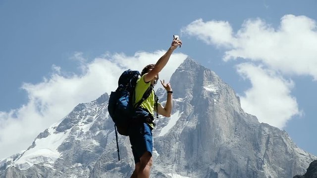 Climber man with a backpack doing a selfie on a smartphone with different emotions. Concept of success, achievement of the goal and victory, slow motion
