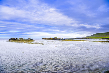 Beautiful rugged volcanic basalt rock Iceland coastline blue skies and low clouds. Green moss and sea grass covered rock formations