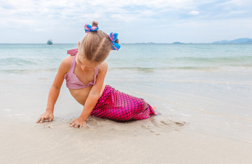 Little beautiful girl dressed in swimsuit as a mermaid sits on the seashore