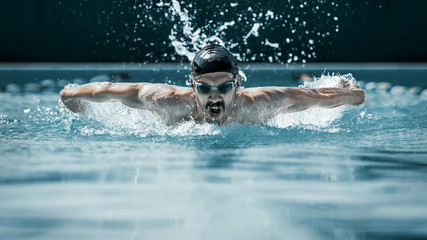 The dynamic and fit swimmer in cap breathing performing the butterfly stroke at pool. The young...