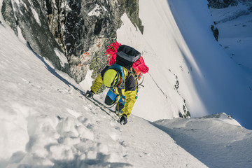 An alpinist climbing steep ice wall. A winter alpine ascent in alpine landscape. Adventure and extreme climb in snow and ice to a summit of a peak. Solo climber in winter mountains.