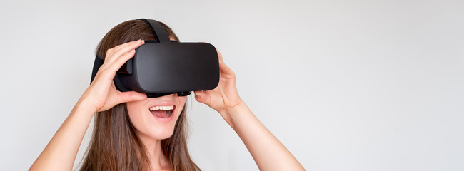 Smiling positive woman wearing virtual reality goggles headset, vr box. Connection, technology, new generation, progress concept. Girl trying to touch objects in virtual reality. Studio shot on gray