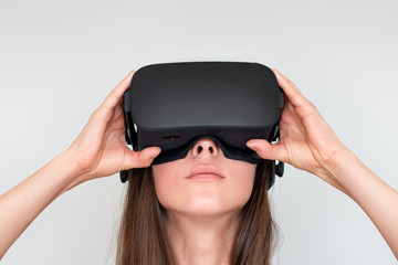 Young woman wearing virtual reality goggles headset, vr box. Connection, technology, new generation, progress concept. Girl trying to touch objects in virtual reality. Studio shot on gray