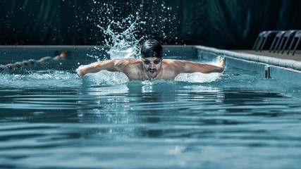 The dynamic and fit swimmer in cap breathing performing the butterfly stroke at pool. The young man. The fitsport, swimmer, pool, healthy, lifestyle, competition, training, athlete, energy concept