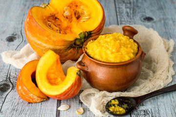        Clay pot with millet porridge and a ripe fresh pumpkin on a napkin on an old wooden table. 