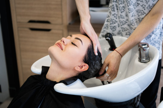 beauty and people concept - happy young woman with hairdresser washing head at hair salon