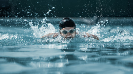 The dynamic and fit swimmer in cap breathing performing the butterfly stroke at pool. The young...