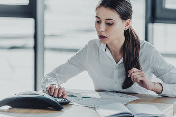 young confident businesswoman with paperwork using conference phone at office