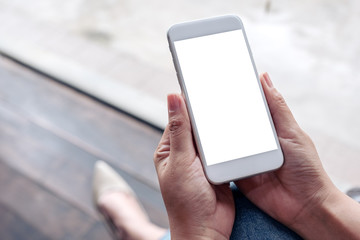 Mockup image of a woman's hand holding and using mobile phone with blank white screen with blur background