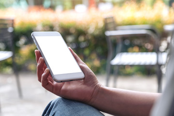 Mockup image of a woman's hand holding and using mobile phone with blank white screen in modern cafe with blur background