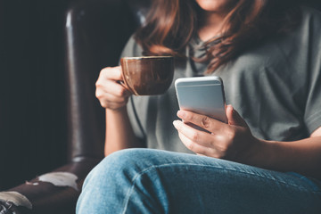 Closeup image of a woman holding , using and touching a smart phone while drinking coffee