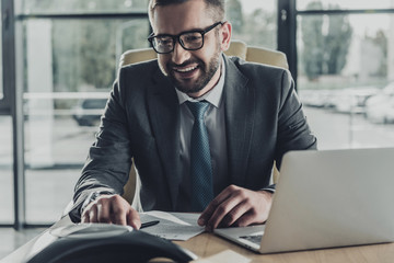 handsome smiling businessman using speakerphone at modern office