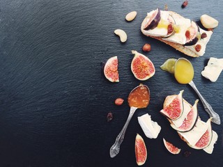                        Bruschetta with cheese, fresh figs, nuts and honey. Sandwiches with cheese, figs and assorted nuts on a black stone board. Top view. Side view.