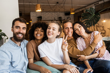 Happy multi ethnic young people looking at camera, smiling diverse friends or students showing peace sign, multicultural millennials posing together at meeting, tolerance and racial equality concept