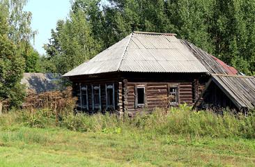 A deserted house without windows is standing among the tall grass