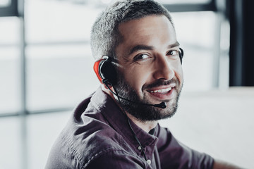 handsome smiling call center worker in headphones with microphone looking at camera