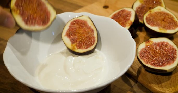 Closeup view of woman hand putting fig pieces into a thyme yogurt bowl to prepare breakfast
