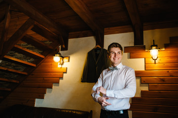 A man in a shirt with a bow tie , wears a metallic silver cufflinks stud on his arm. On the...