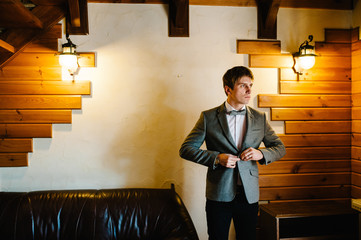 Man fastens the buttons. The groom in a shirt, bow tie is standing in room. The man is wearing a...