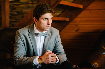 Serious, Imposing well dressed in suit man in a luxurious apartments with classic wooden interior. Men's fashion. Sexy groom in tuxedo and bow tie, posing in wedding morning.