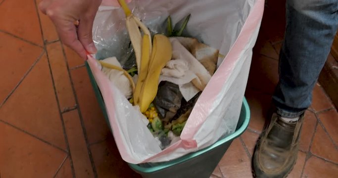 Man removes a plastic bag of trash from a kitchen plastic garbage bin