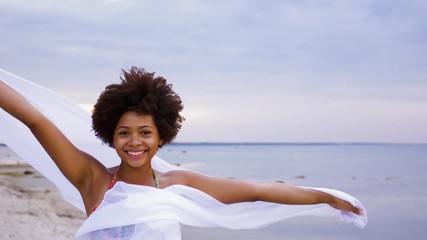 people and leisure concept - happy african american young woman with shawl waving in wind on summer beach
