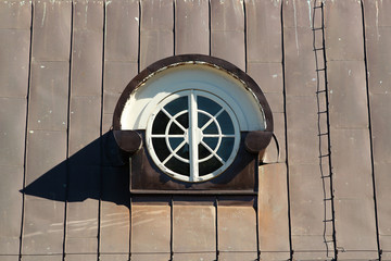 Round attic window in a metal covered roof