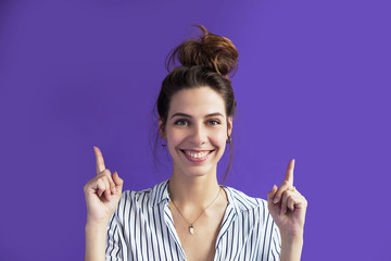 A calm, cute young woman points her fingers at something above her head to something important,...