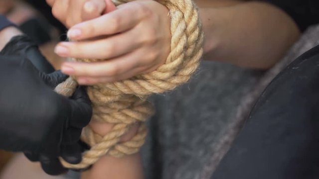 Criminal tying kidnapped female hands with rope, illegal human trafficking
