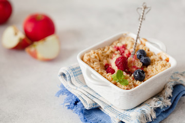 Traditional British apple crumble on portion baking dish with fresh berries