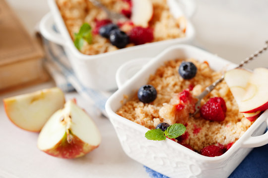 Traditional British apple crumble on portion baking dish with fresh berries
