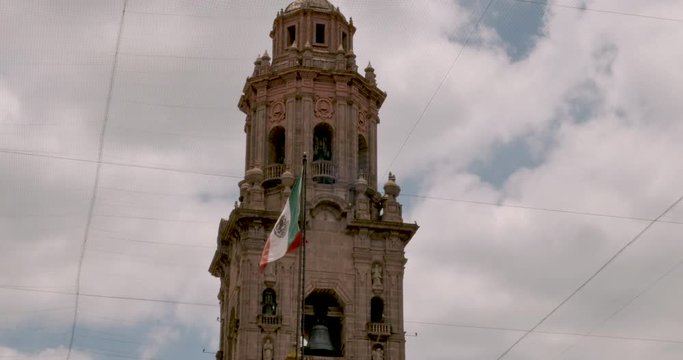Mexican flag flying next to a bell tower of the Morelia Cathedral