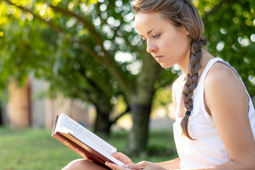 Obraz premium Christian worship and praise. A young woman is reading the bible in the early morning with sun in the background.