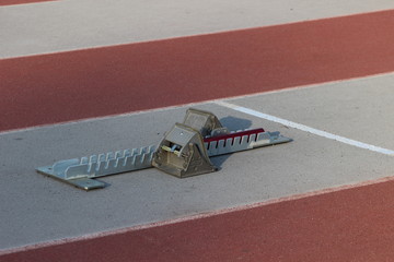 Athletic start block on dark red tartan track