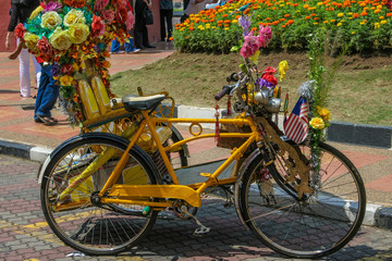 Fototapeta na wymiar Great close-up of a yellow trishaw nicely decorated with colourful flowers, a flag and other trinkets which is a popular transportation for tourists in Malacca, Malaysia.