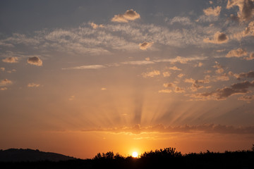 Sunset with sun almost hidden and shadows on the clouds and blue sky