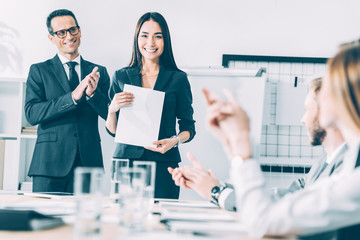 rewarded happy asian manageress holding blank paper while colleagues clapping to her