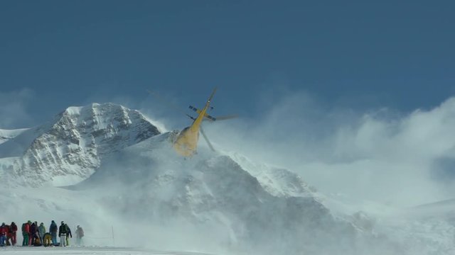 Mountain Helicopter Taking Off. Helicopter on the top of the mountain Takes off from ground. Heli Skiing Helicopter. Group of skiers waiting for helicopter. Slow Motion. Skiers and snowboarders