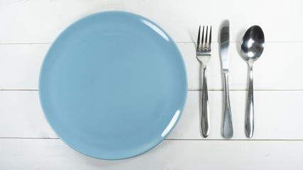 Empty blue dishes plate  fork and knife on a white wooden table background, Top view, Free space for text..