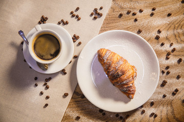 Croissant and coffee on a wooden table, coffee grains scattered on a table