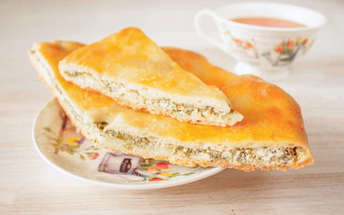 Oriental pastry fresh hot traditional Ossetian pie with homemade cheese, spinach and herbs cut into pieces in saucer with cup of tea. Close-up, selective focus.