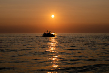The silhouette of a ship sailing on the sea on the backdrop of the setting sun and a sun track on the water