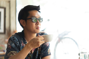 A hipster boy with sunglasses is drinking hot coffee.