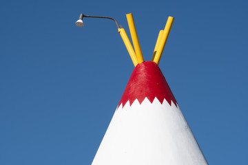 Top half abstract view of a wigwam structure made of concrete and rebar. Painted red white and yellow against blue sky background © MelissaMN