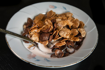 Breakfast. Sereal flakes  in white plate with milk. Black table.
