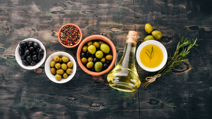 A set of olives and olive oil and rosemary. Green olives and black olives. On a black wooden background. Free space for text.