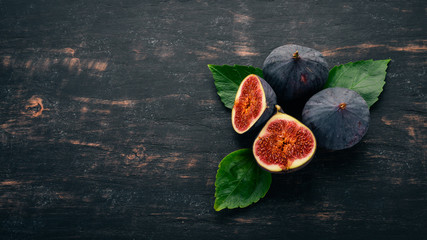Fresh figs with leaves on a black wooden table. Free space for text. Top view.